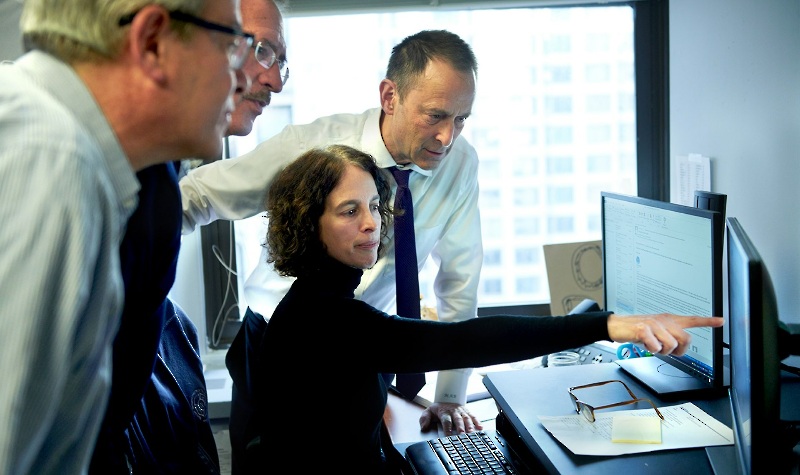 A group of Attorneys Leans Over a Woman Pointing At Her Computer Screen